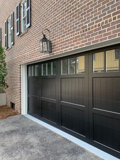 a black garage door with windows on the side of a brick building next to a tree