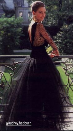 a woman in a black dress standing on a balcony