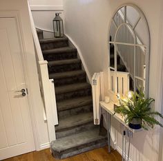 an entryway with stairs, mirror and potted plant on the table next to it