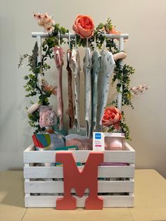 the letter m is placed in a crate with clothes and flowers