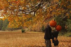 two people standing under a tree with pumpkins on their heads