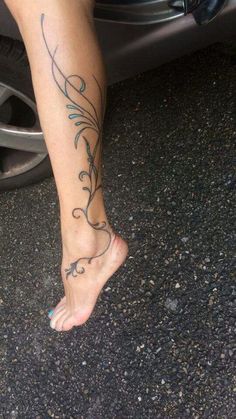 a woman's foot with a tattoo on the side of her leg and in front of a car