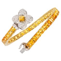 The yellow sapphire bracelet features a row of especially calibrated baguette princess-cut yellow sapphires (approximately 19 carats) flanked by a bridge set with round diamonds. The golden sapphires are of fiery color and crystalline texture. The clasp consists of a flower design set with round diamonds. The total weight of round diamonds of top quality (F/G-VVS) is approximately 1 carat. The design is accented by the use of both white and yellow 18 carat gold. The bracelet was handmade in Ital Diamond Bracelet Design, Bracelet Tennis, Bracelets Design, White Gold Sapphire, Fancy Diamonds, Sapphire Bracelet, Elegant Bracelet, Yellow Gold Bracelet, A Bridge