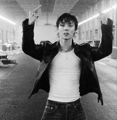 a man with his hands in the air standing on a city street while wearing jeans and a leather jacket