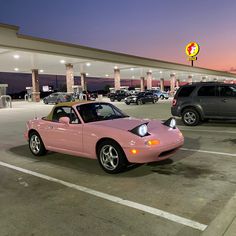 a pink sports car parked in a parking lot next to a gas station at night