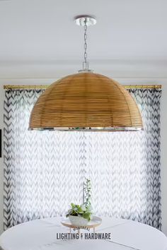 a round table with a plant on it in front of a window covered by curtains