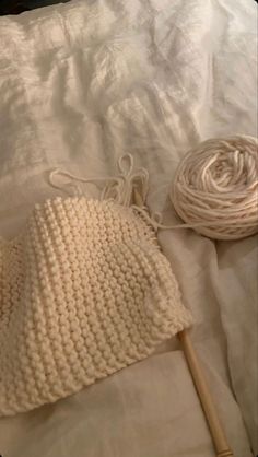 a white crocheted hat and ball of yarn on a bed