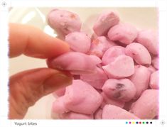 a hand is picking up some pink doughnuts from a white bowl on the table