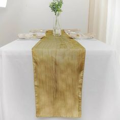 a vase with flowers on top of a white table cloth draped over the place setting