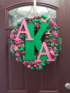 a green and pink wreath with the letter k hanging on it's front door