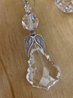 a clear crystal necklace with an angel wing hanging from it's side on a wooden surface