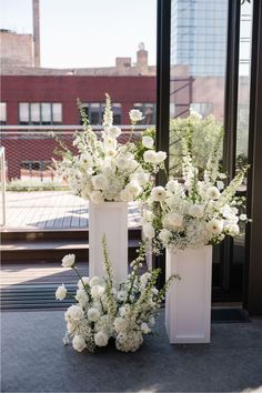 two tall vases with white flowers are sitting on the ground in front of a window