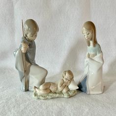 two figurines are sitting next to each other on a white surface, one is holding a stick and the other is laying down