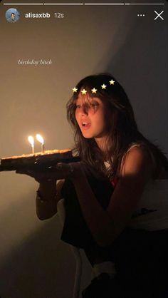 a woman holding a cake with lit candles on it in front of her face and looking at the camera