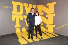 a man and woman standing in front of a wall with the words down town written on it