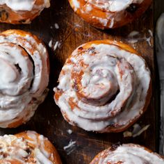 cinnamon rolls with icing sitting on top of a wooden cutting board