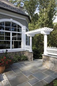 a house with a white pergolan and flowers in the front yard