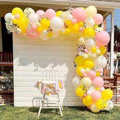 a bunch of balloons that are in the grass near a chair and table with a cake on it