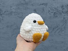 a hand holding a crocheted white and yellow bird