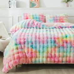 a bed with a colorful comforter and pillows on it in a room next to a white chair