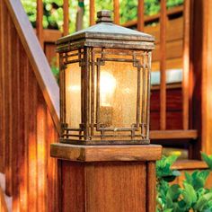 an outdoor lamp on the steps in front of a wooden railing and stairs with green plants