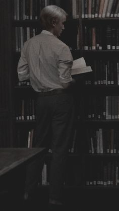 a man standing in front of a bookshelf with a book on his lap