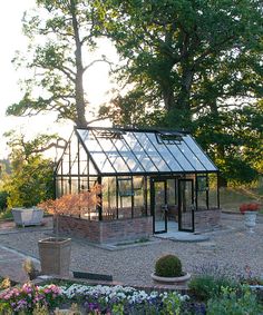 a small glass house surrounded by flowers and trees