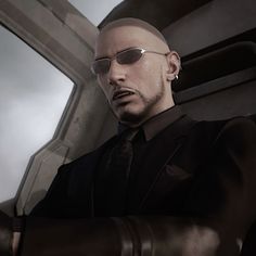 a bald man in a suit and sunglasses standing next to a window with cloudy sky behind him