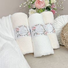 three white towels are sitting next to a vase with flowers in it and on the bed