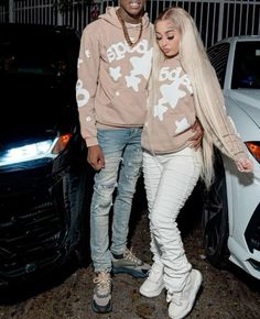 a man and woman standing next to each other in front of a white car wearing matching sweatshirts