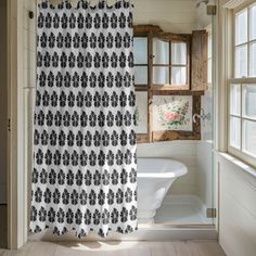 a bathroom with a shower curtain that has black and white designs on it, in front of a window