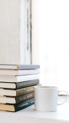 a stack of books sitting next to a coffee cup on top of a white table