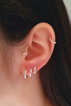 a woman's ear with three small silver hoops