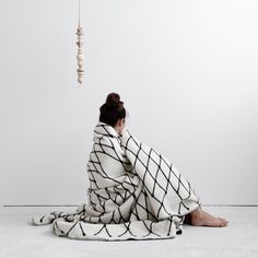 a woman sitting on the floor under a white and black blanket looking at a kite