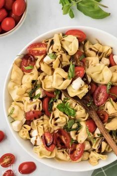 a white bowl filled with pasta and tomatoes next to fresh basil on top of a marble counter