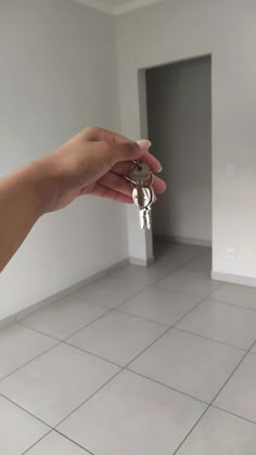 a hand holding keys in front of a white tiled floor and wall with an open door