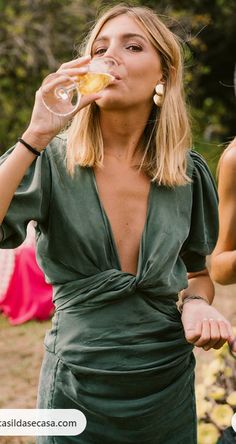 a woman in a green dress drinking from a wine glass