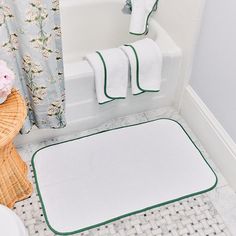 a white bathroom with green trimmings on the bath mat and rug in front of the tub