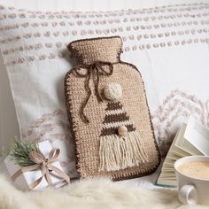 a crocheted bag sitting on top of a pillow next to a cup of coffee