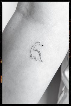 a small dinosaur tattoo on the left side of the arm, with a tiny heart in it