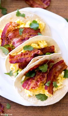 three breakfast tacos with bacon, eggs and cilantro on a white plate