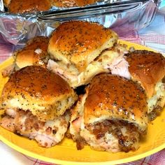 several sandwiches on a yellow plate next to some silver trays with food in them