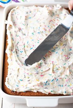 someone is cutting into a cake with white frosting and sprinkles