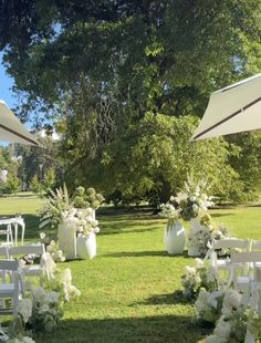 an outdoor ceremony setup with white chairs and flowers on the grass, under umbrellas