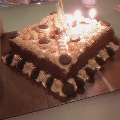 a square cake with lit candles sitting on top of a wooden table next to cookies