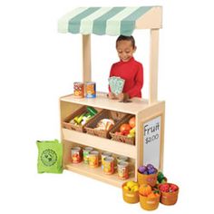 a young boy standing in front of a fruit stand with fruits and vegetables on it