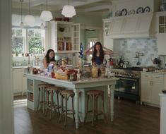 two women standing in a kitchen with lots of food on the counter and stools