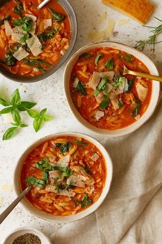 three bowls of soup with basil, parmesan cheese and bread on the side