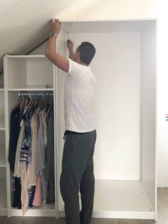 a man standing in front of a white closet with clothes hanging on the walls and shelves