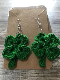 a pair of green crocheted clover earrings sitting on top of a piece of paper